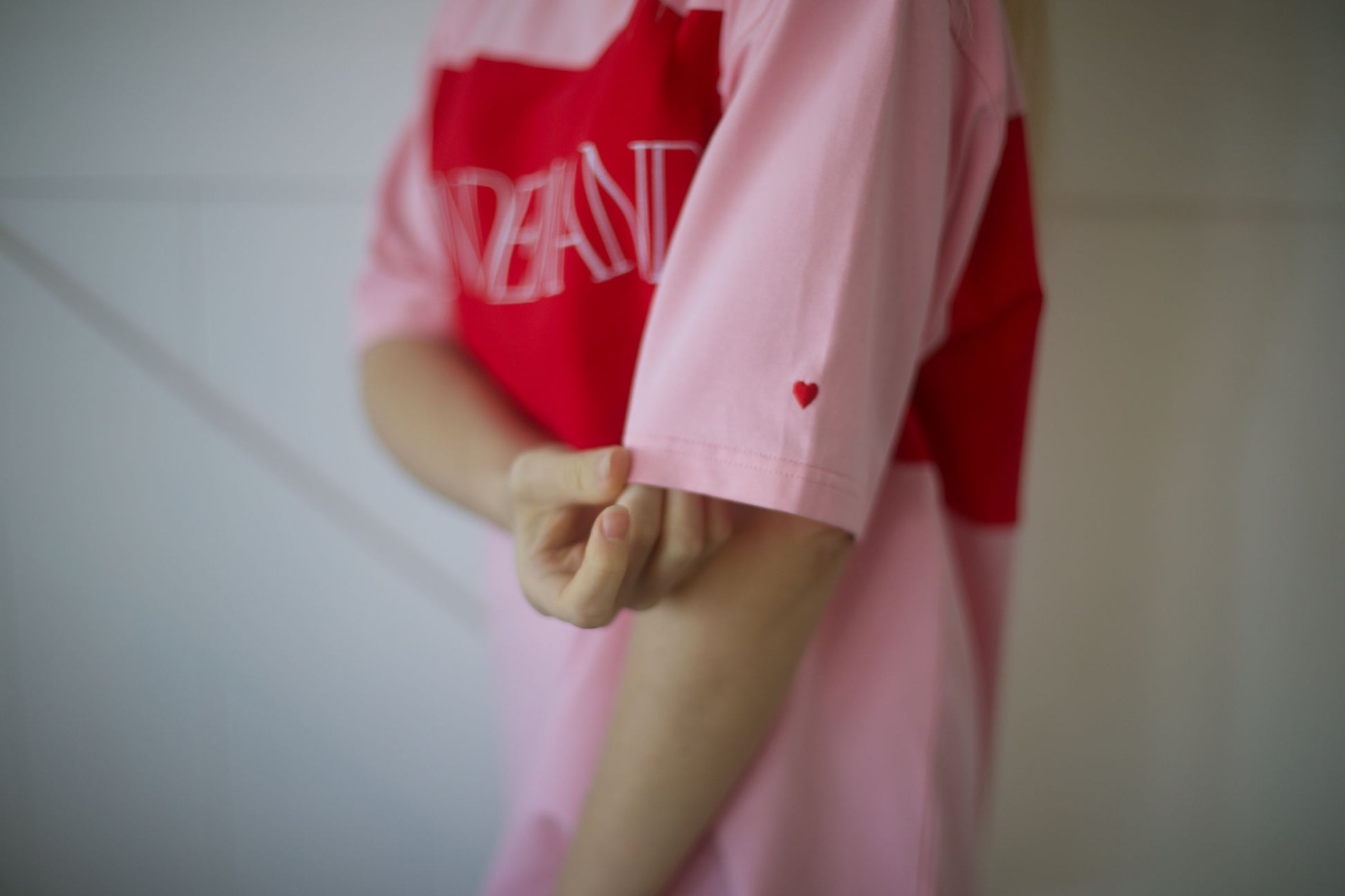 Close-up of the signature embroidered heart on the left sleeve of the pink On Demand breastfeeding t-shirt.