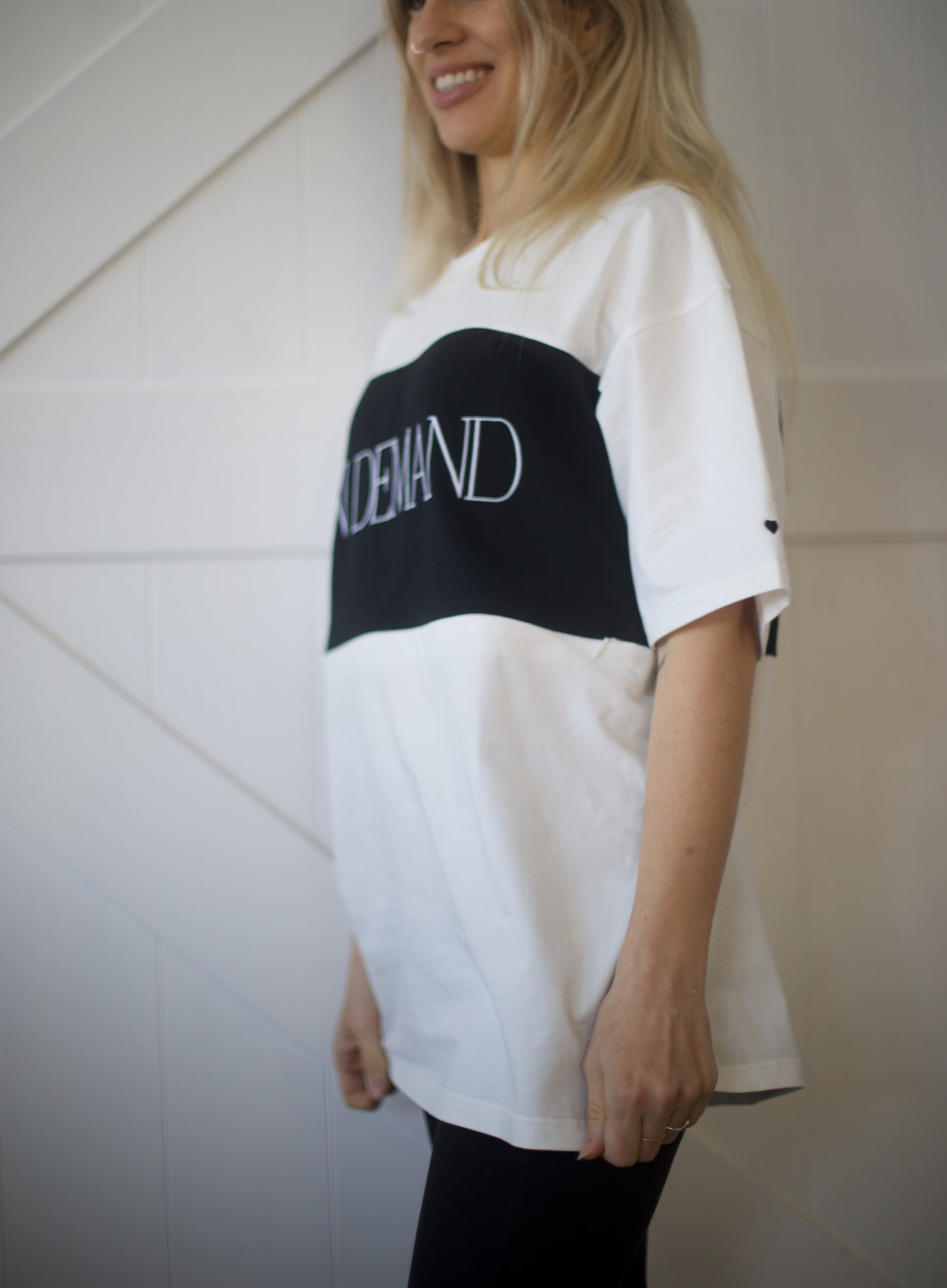 Side view of oversized On Demand breastfeeding t-shirt in white and black with drop shoulders and embroidered heart on sleeve