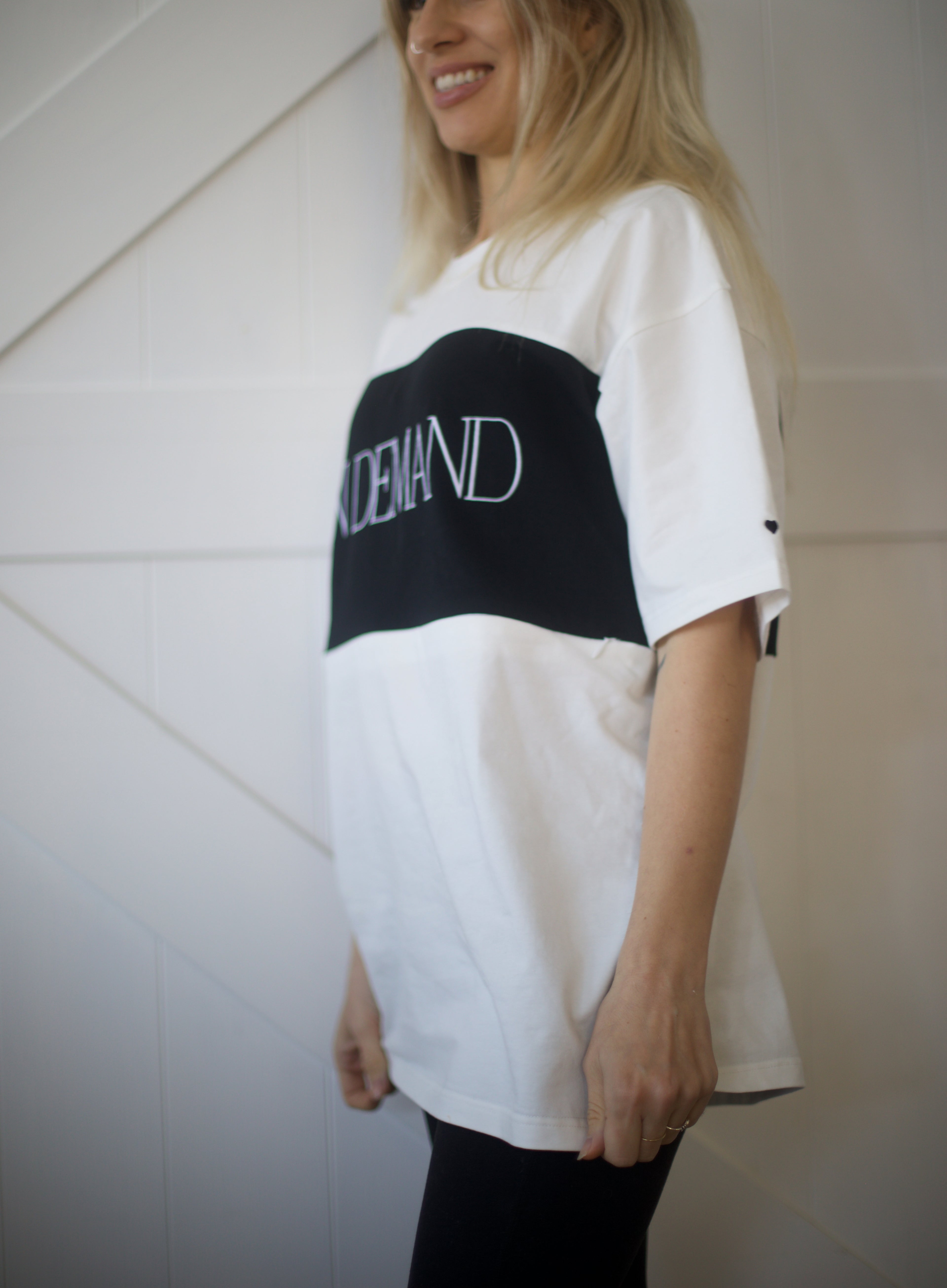 Side view of oversized On Demand breastfeeding t-shirt in white and black with drop shoulders and embroidered heart on sleeve
